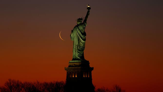 A five percent illuminated waning crescent moon rises behind the Statue of Liberty as the sun rises in New York City on March 27, 2025, as seen from Jersey City, New Jersey.
